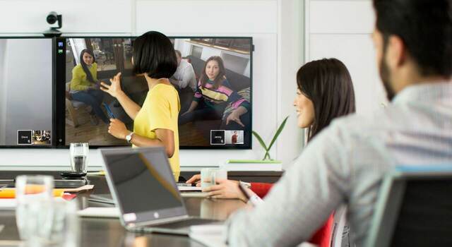 Pessoas sentadas em uma sala de reunião conectadas por videoconferência